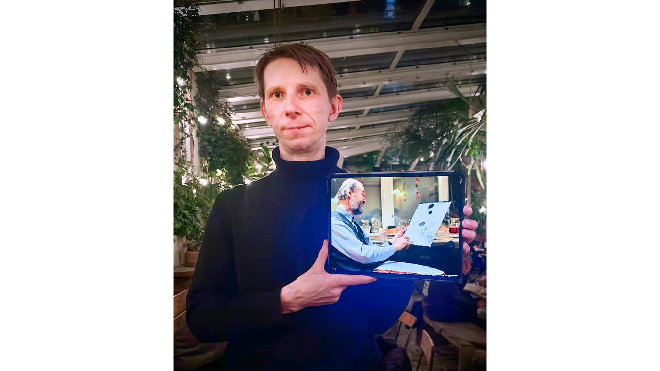 Serietecknaren Joonas Sildre och en bild av kompositören Arvo Pärt som tittar på Sildres första idéskiss till boken. Kafé Magasinet i Göteborg, 1 februari 2026. Foto: Susanne Willgren Lamm