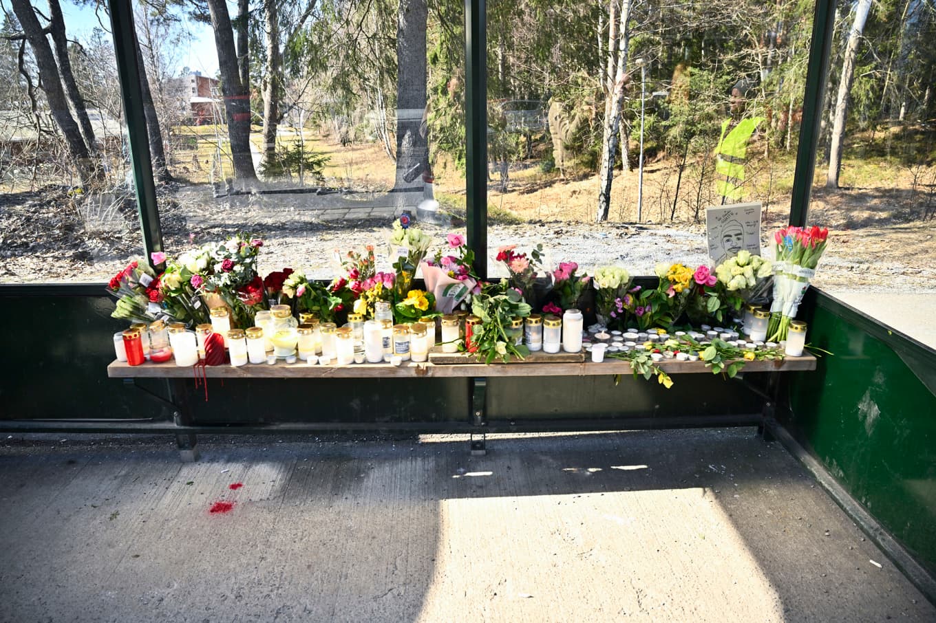 Minnesplats med tända ljus och blommor vid busshållplatsen där en man i 18-årsåldern sköts till döds på en SL-buss. Bild från i fredags. Foto: Fredrik Sandberg/TT