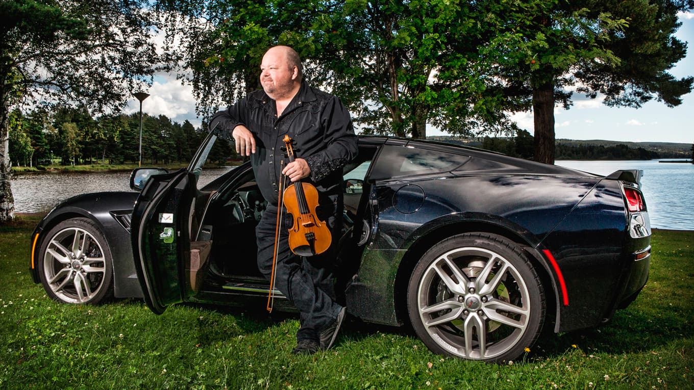 Spelmannen Kalle Moraeus med fiol och bil av sentida modell. Orsasjön i bakgrunden. foto: Janne Danielsson/SVT