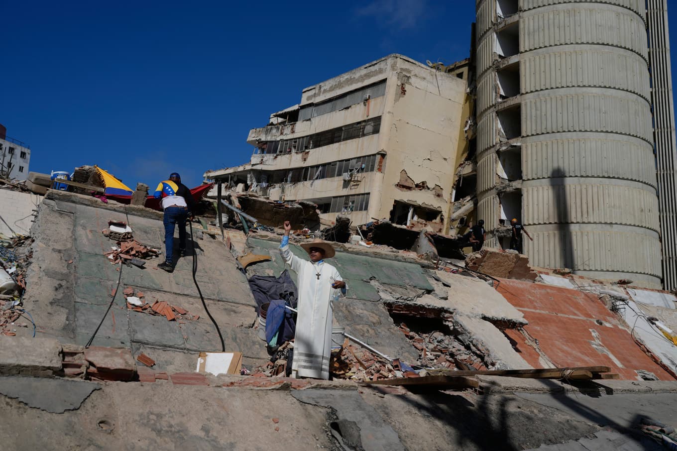 En katolsk präst står bland rasmassorna från bostadshus. Bild från i fredags. Foto: Ariana Cubillos/AP/TT