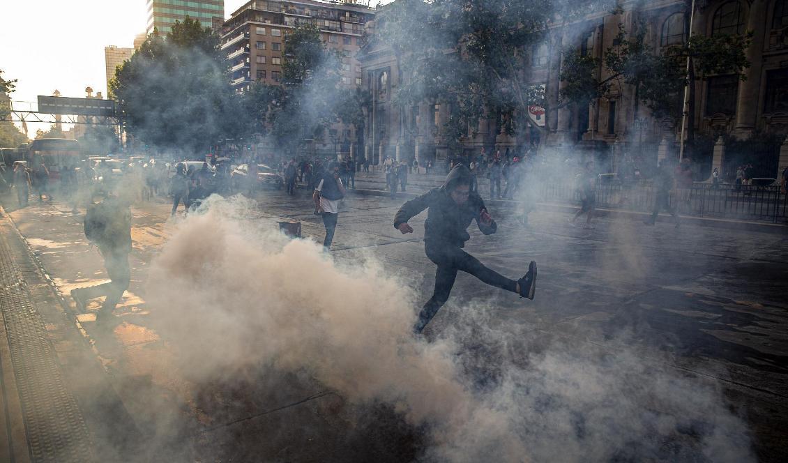 En demonstrant sparkar på en tårgasgranat under fredagens protester i Santiago. Foto: Esteban Felix/AP/TT