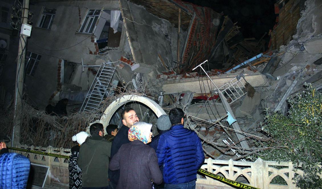 Människor framför en byggnad som rasat samman i staden Elazig i östra Turkiet. Minst fyra människor dog i en kraftig jordbävning. Foto: AP/TT