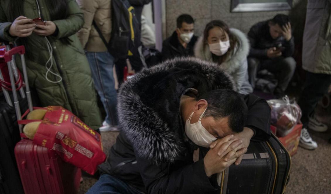 En kinesisk man i skyddsmask sover på en tågstation i Peking i väntan på avgång för att åka och fira det kinesiska nyåret. Peking, Kina, den 23 januari 2020. Foto: Kevin Frayer/Getty Images
