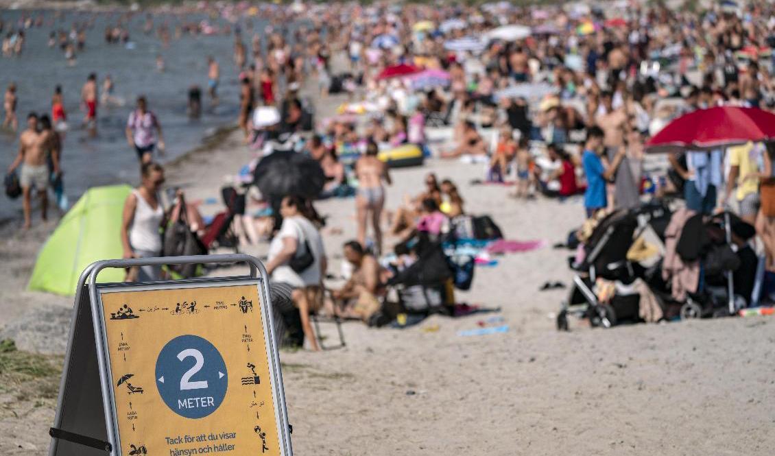 En skylt påminner om att hålla avstånd på stranden i Lomma, Skåne. Polisen i Sverige har fått in många samtal om trängsel på badstränder. Foto: Johan Nilsson/TT