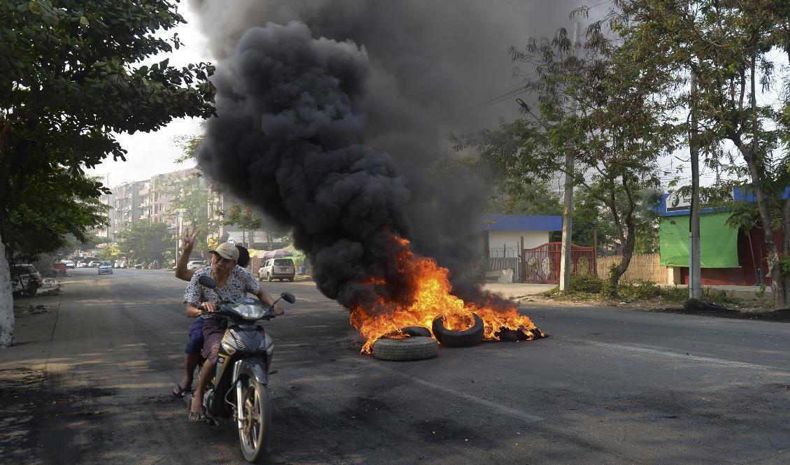 Juntakritiska demonstranter åker förbi en brinnande barrikad i Rangoon. Foto: AP/TT