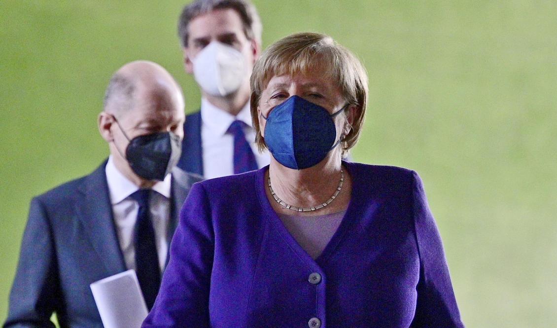 Tysklands avgående förbundskansler Angela Merkel, med tillträdande förbundskansler Olaf Scholz strax bakom, har i samråd med förbundsländernas ledare beslutat att skärpa kraven om vaccinering. Foto: John Macdougall/poolfoto via AP/TT