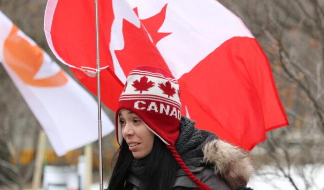 En demonstrant bär en stor kanadensisk flagga i Queen’s Park i centrala Toronto den 5 mars 2022. Foto: Annka Wang