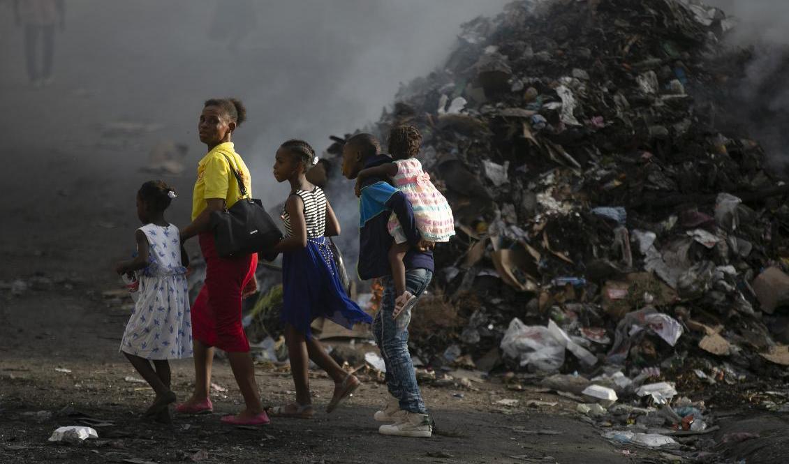 En familj framför en rykande sophög i Port-au-Prince i onsdags. Foto: Odelyn Joseph/AP/TT