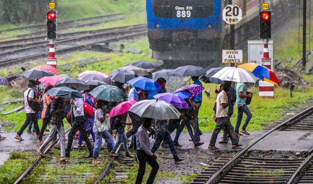 Fotgängare går över en järnvägskorsning i Colombo, Sri Lanka. De har sina paraplyer uppfällda för det regnar hårt.  Foto: Ishara S. Kodikara/AFP via Getty Images